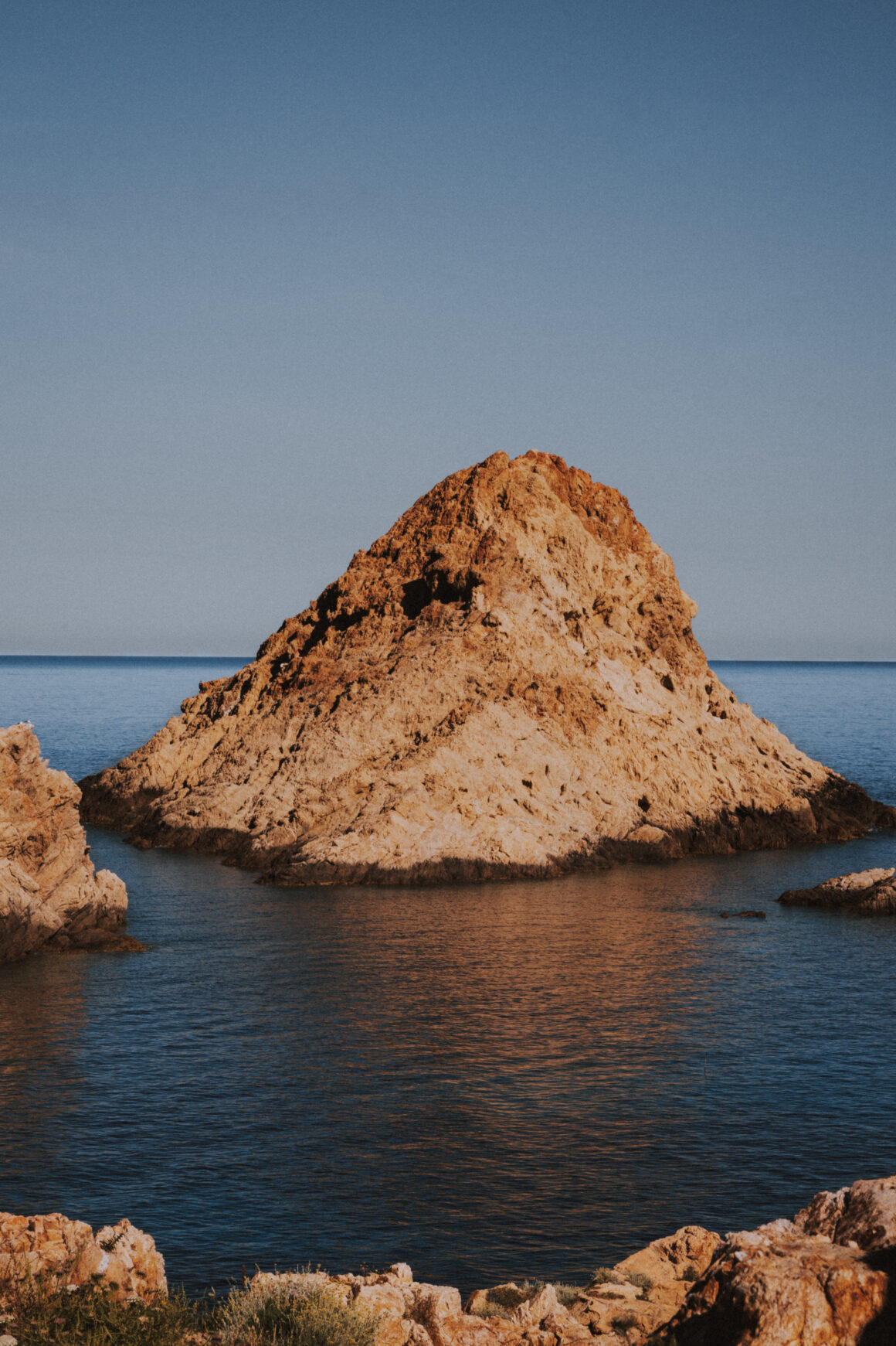 Photographe de tourisme et de paysage, vue sur l'îlot rocheux emblématique de L'Île-Rousse en Balagne en Corse, mer Méditerranée et roches ocres. Photo sélectionnée par Maquis Magazine.