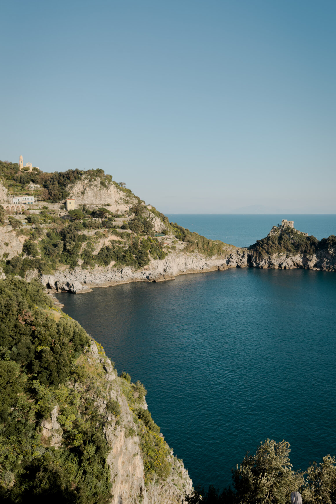 Reportage photographique de Claire-Emmanuelle Hamelin montrant un paysage de la Côte Amalfitaine en Italie : falaises escarpées, mer Méditerranée bleue et architecture côtière typique sous une lumière naturelle.