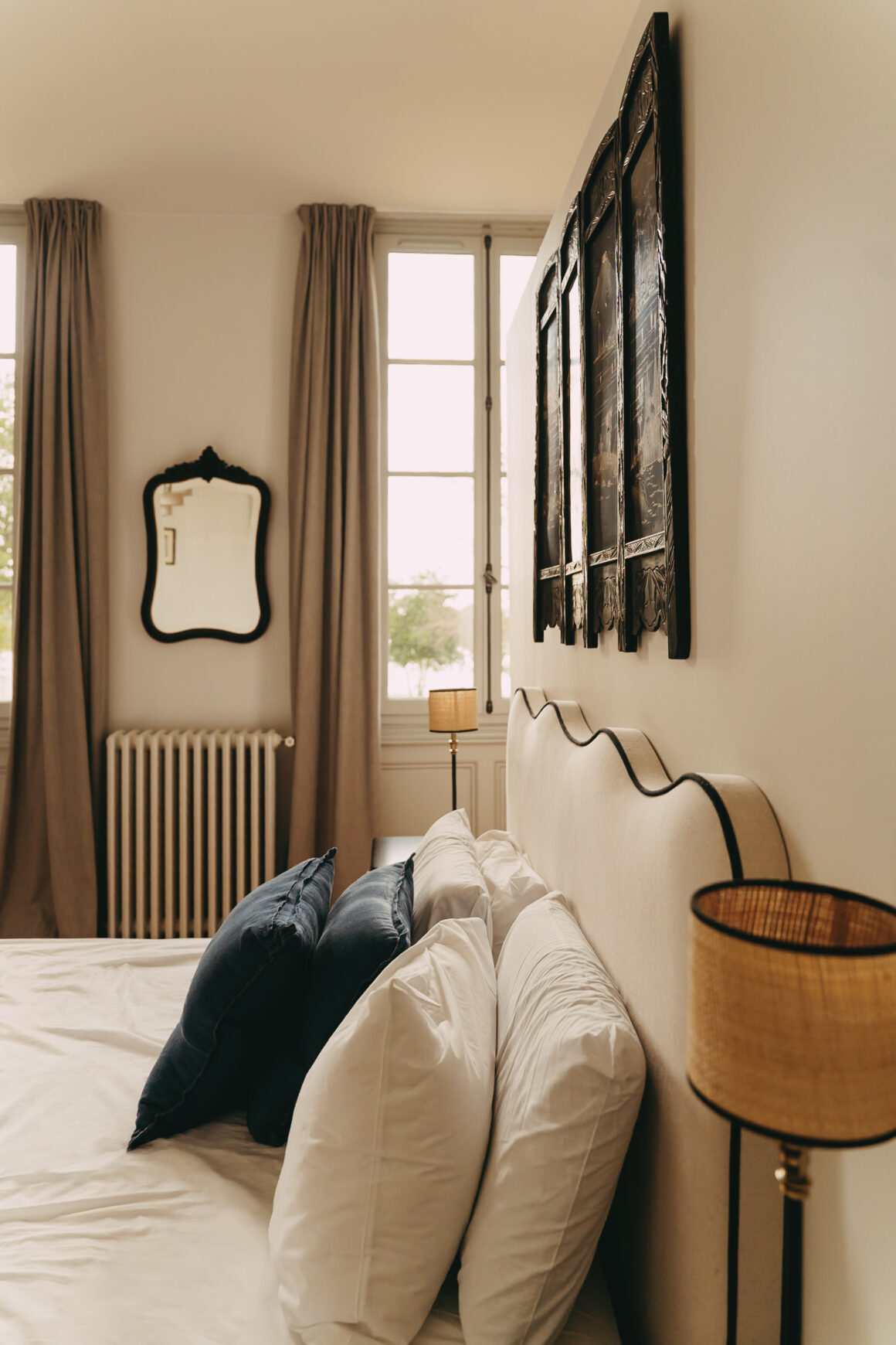 Chambre du Château Larteau avec tête de lit claire, coussins bleu marine et panneaux décoratifs anciens.