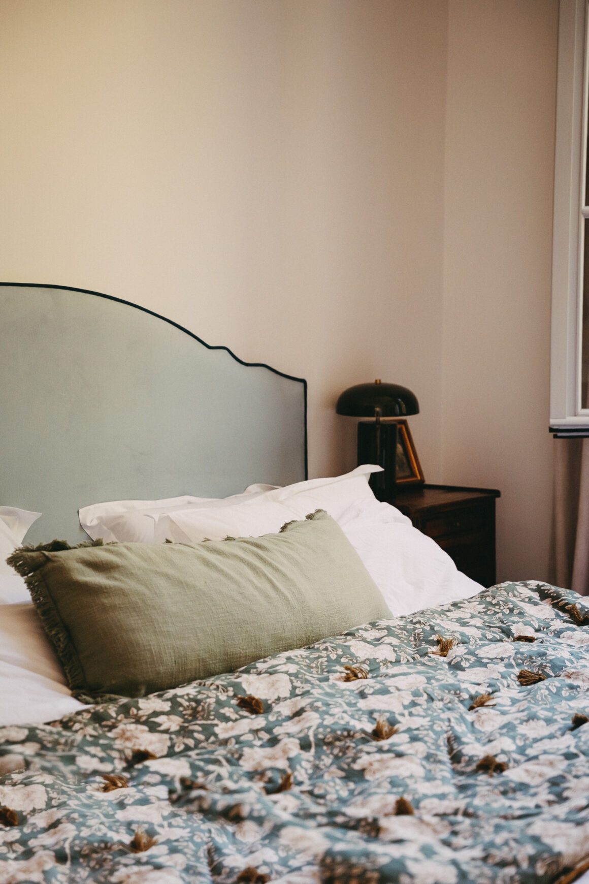 Chambre du Château Larteau avec tête de lit vert pâle et couvre-lit à motifs floraux.
