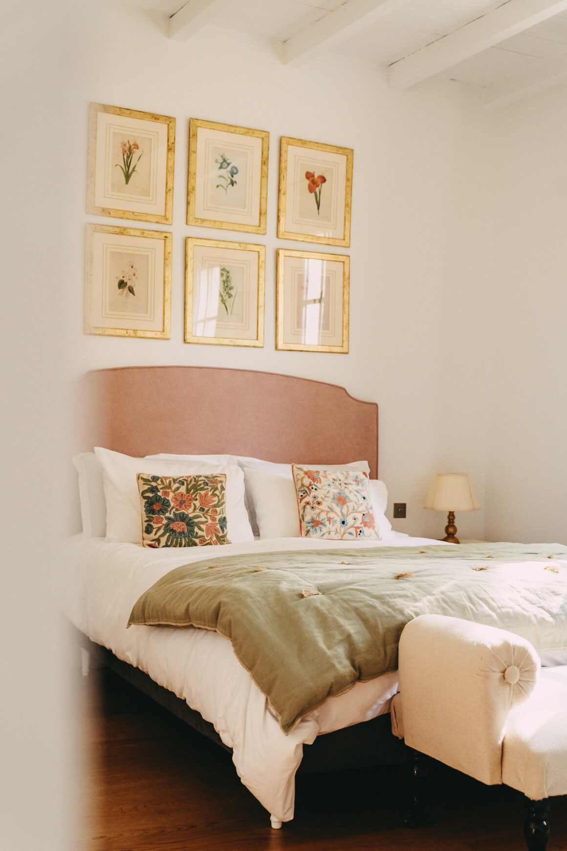 Chambre du Château Larteau en Gironde, avec tête de lit rose, linge de lit aux tons verts et illustrations botaniques.