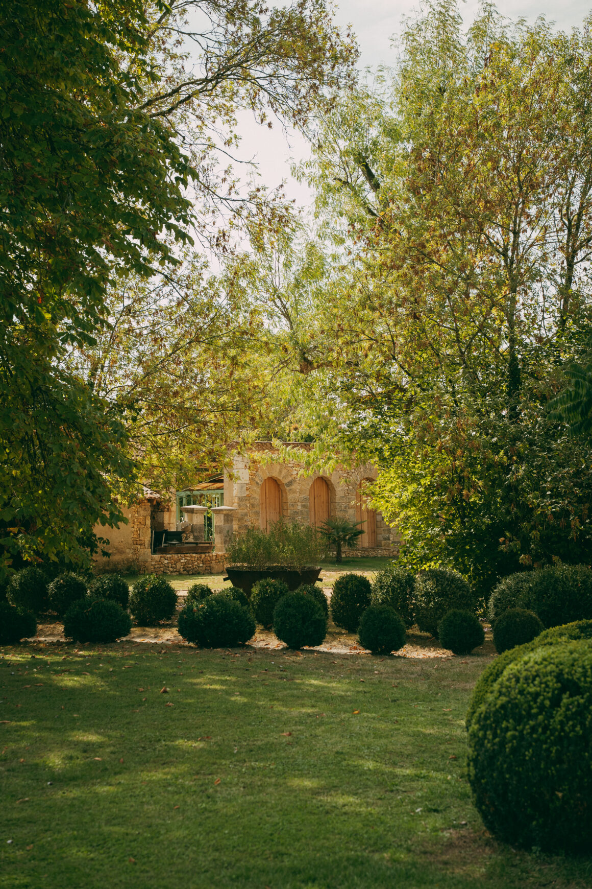Jardin arboré du Domaine de Lavernelle, avec ses buis taillés et ses bâtiments en pierre.