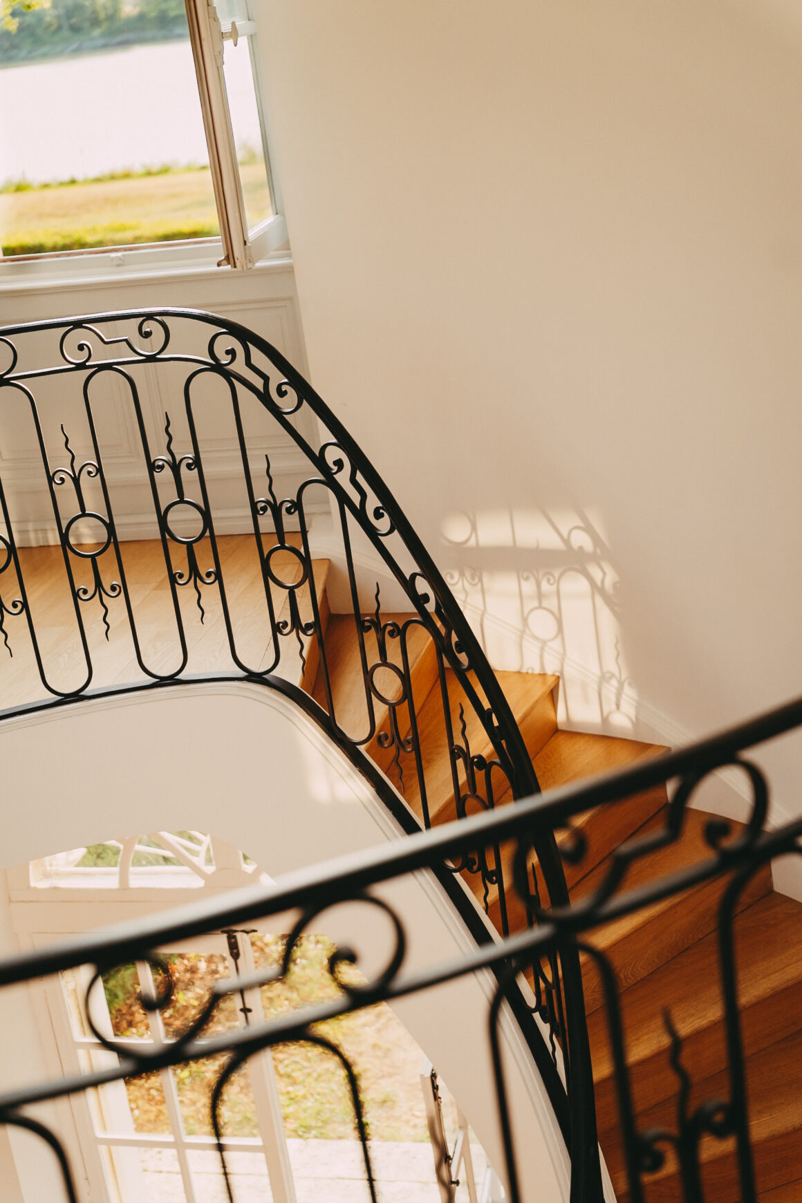 Escalier courbe en bois et ferronnerie noire du Château Larteau, éclairé par la lumière naturelle.