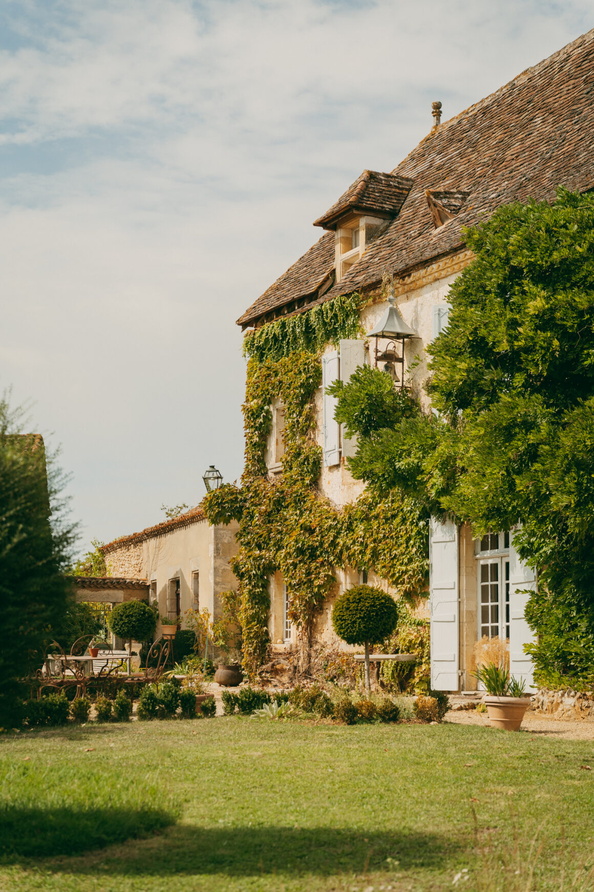 Façade en pierre couverte de vigne vierge, aux volets blancs et à la toiture en tuiles anciennes, au Domaine de Lavernelle.