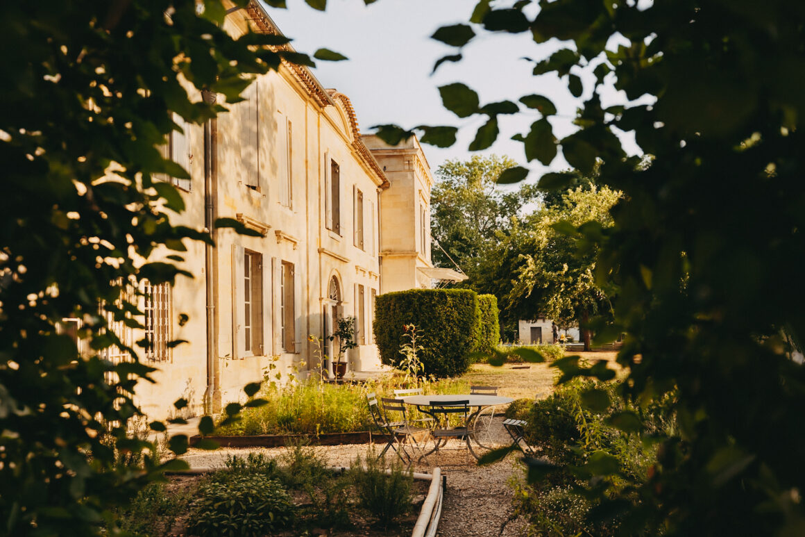 Façade du Château Larteau et mobilier de jardin encadrés par le feuillage.