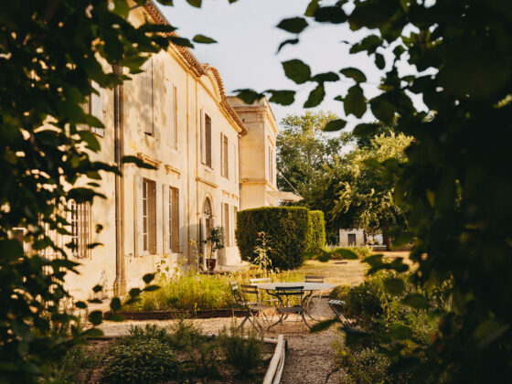 Façade du Château Larteau et mobilier de jardin encadrés par le feuillage.