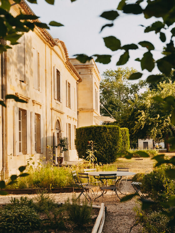 Façade du Château Larteau et mobilier de jardin encadrés par le feuillage.