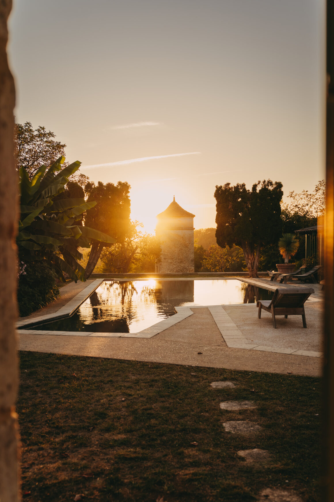 Piscine du Domaine de Lavernelle à l’heure dorée, avec un pigeonnier en pierre et des transats entourés de végétation.
