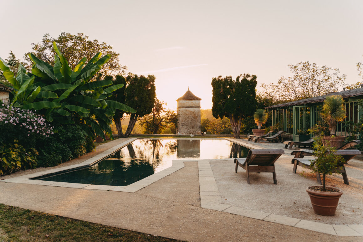 Vue panoramique de la piscine du Domaine de Lavernelle au coucher du soleil, avec son pigeonnier, ses transats et ses jardins.