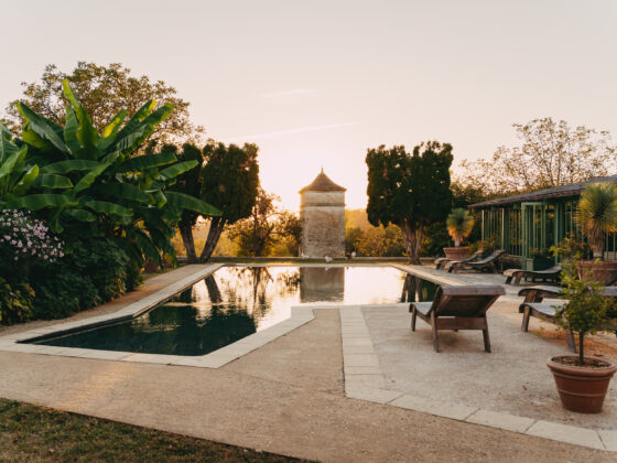 Vue panoramique de la piscine du Domaine de Lavernelle au coucher du soleil, avec son pigeonnier, ses transats et ses jardins.