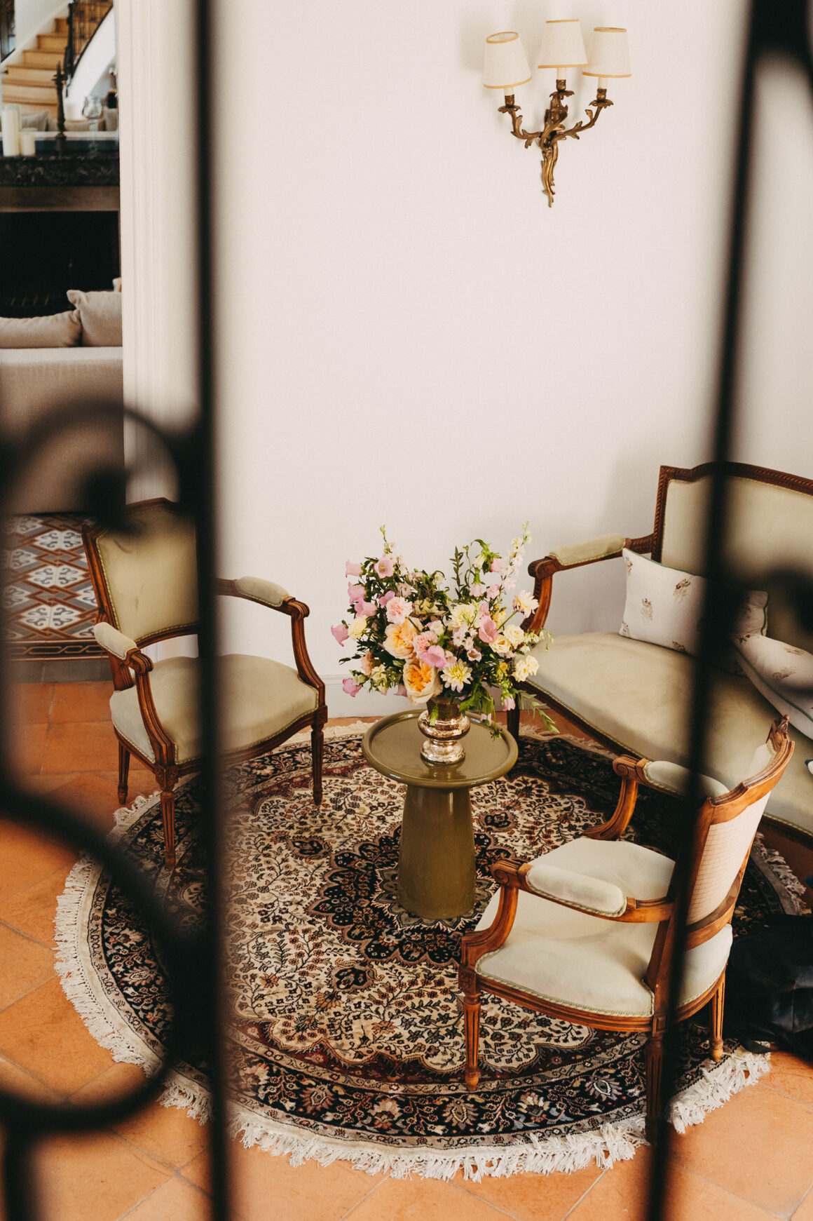 Salon du Château Larteau vu depuis l’escalier, avec mobilier ancien, tapis et bouquet de fleurs.