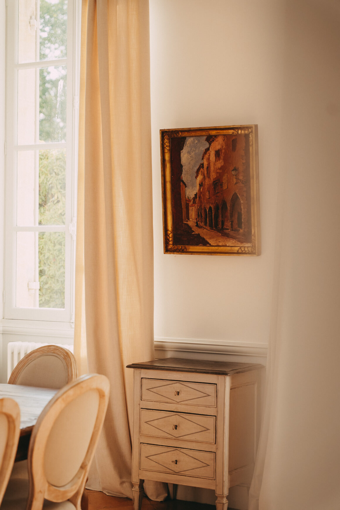 Tableau ancien encadré d’or et petite commode dans la salle à manger du Château Larteau, près de Bordeaux.