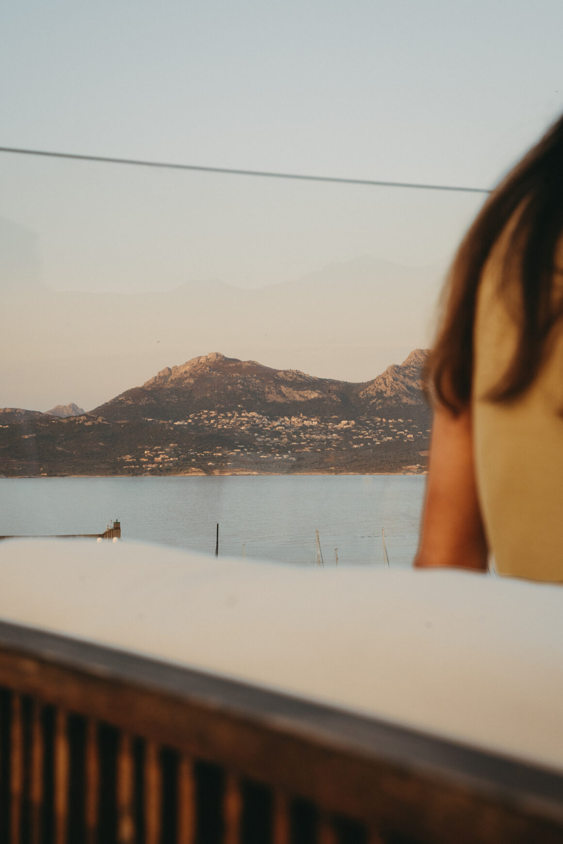 Vue sur la baie et les montagnes de Calvi depuis la terrasse de l’Hôtel L’Acquale, avec une silhouette au premier plan.